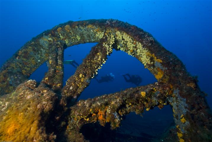 Épave sous-marine à Hyères avec une roue métallique recouverte de coraux, explorée par des plongeurs dans les profondeurs.