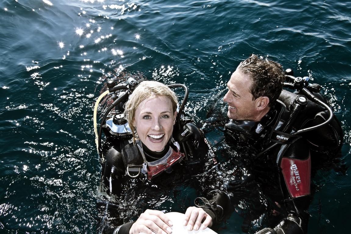 Deux plongeurs souriants à la surface de l'eau, prêts pour une aventure sous-marine.